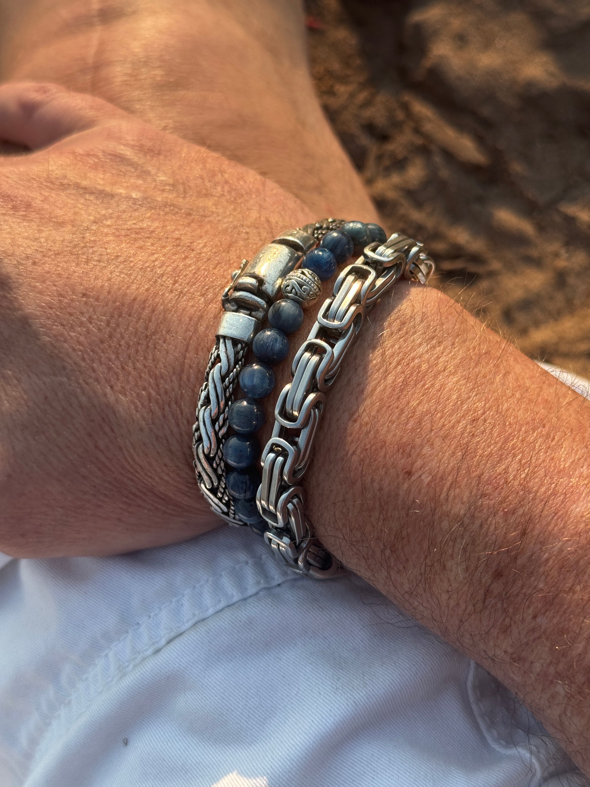 Close-up of a wrist wearing multiple bracelets with a blurred background. Features the Arts of Dreaming Kyanite Bracelet -  made of blue Kyanite beads and a carved silver bead accent for lucid dreaming practice. 